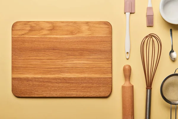 Top view of empty wooden chopping board and cooking utensils on yellow background — Stock Photo