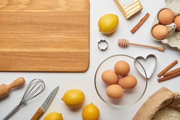 Top view of empty wooden cutting board and bakery ingredients on grey background — Stock Photo