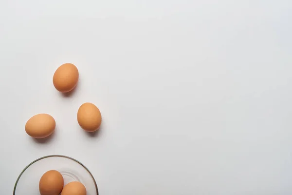 Top view of organic scattered eggs and glass bowl on grey background — Stock Photo