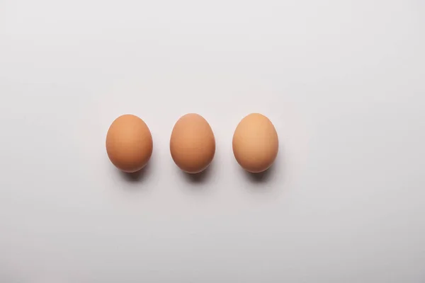 Flat lay with three organic eggs on grey background — Stock Photo