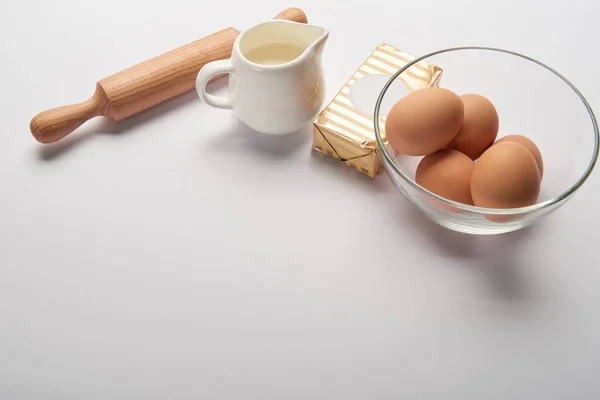 Rolling pin, jar with milk, butter and eggs in bowl on grey background with copy space — Stock Photo