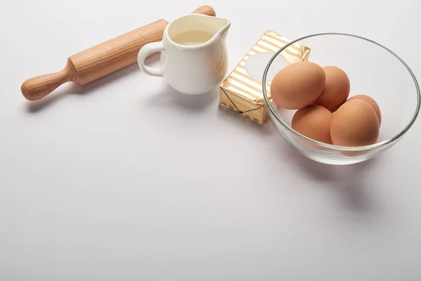 Rouleau à pâtisserie, bocal avec lait, beurre et oeufs dans un bol sur fond gris avec espace de copie — Photo de stock