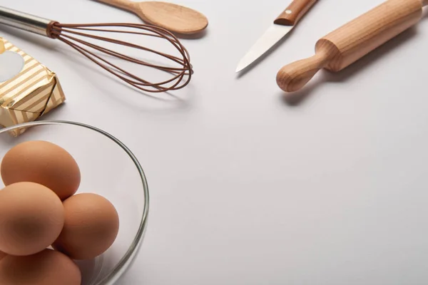 Close up of cooking utensils, butter and eggs in bowl on grey surface — Stock Photo