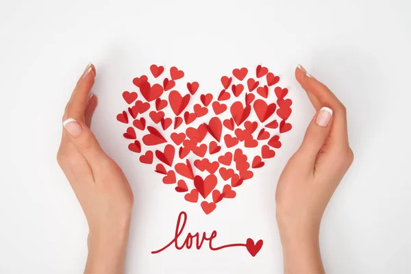 Cropped view of female hands near heart shaped arrangement of small red paper cut hearts with 