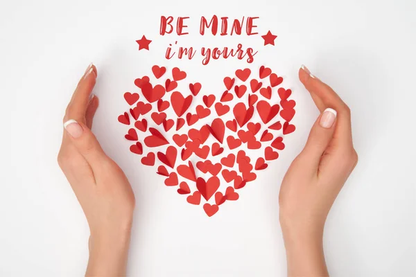 Cropped view of female hands near heart shaped arrangement of small red paper cut hearts with 