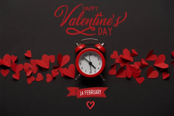 Top view of clock and red paper cut decorative hearts on black background with 