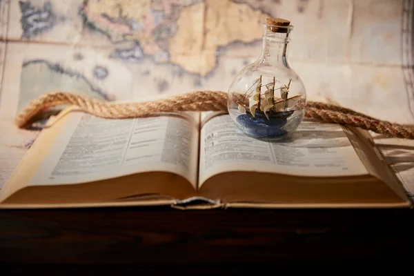 Selective focus of toy ship in glass bottle, book, map and rope on table — Stock Photo