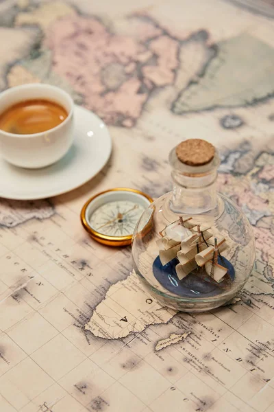 Enfoque selectivo de la taza de café, brújula y barco de juguete en botella de vidrio en el mapa - foto de stock