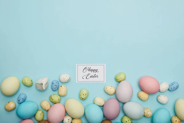 Top view of toy bunny, painted easter and quail eggs and card with happy easter lettering — Stock Photo