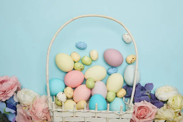 Vue du dessus des oeufs de poulet et de caille de Pâques dans le panier de paille et les fleurs — Photo de stock