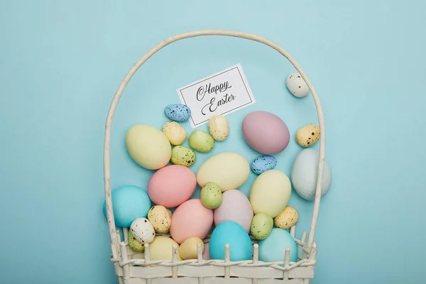 Top view of painted easter chicken and quail eggs in straw basket, card with happy easter lettering — Stock Photo
