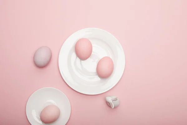 Ansicht von Spielzeughase, bemalte Ostereier auf Untertasse und Teller auf rosa Hintergrund — Stockfoto