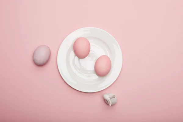 Vista superior del conejito de juguete, huevos de Pascua pintados en plato sobre fondo rosa - foto de stock