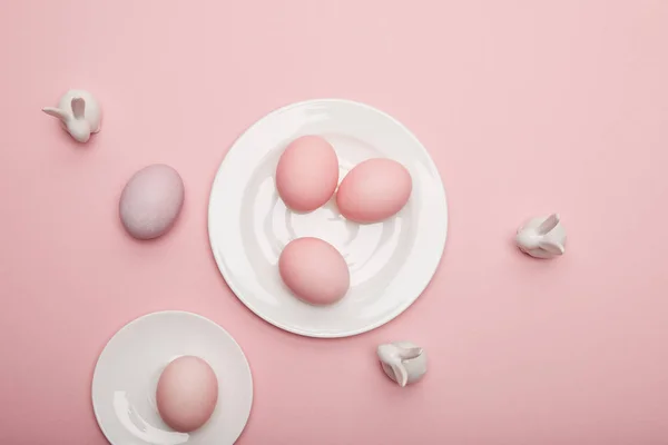 Vue du dessus des lapins jouets, oeufs de Pâques sur soucoupe et assiette sur fond rose — Photo de stock