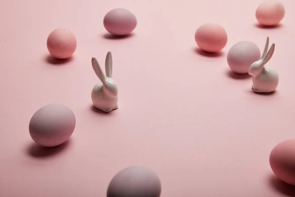 Игрушечные кролики и окрашенные пасхальные яйца на розовом фоне с копировальным пространством — стоковое фото