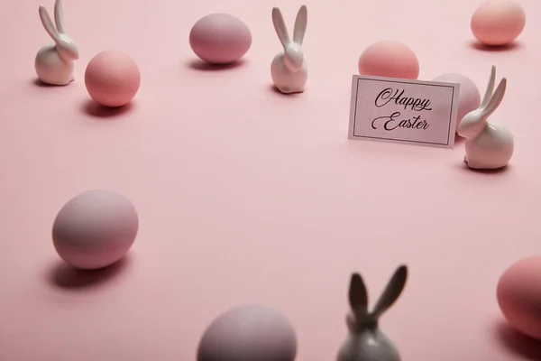 Coelhinhos de brinquedo, cartão com letras páscoa feliz e ovos de Páscoa no fundo rosa com espaço de cópia — Fotografia de Stock