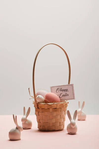 Easter chicken and quail egg in straw basket, card with happy easter lettering and toy rabbits — Stock Photo