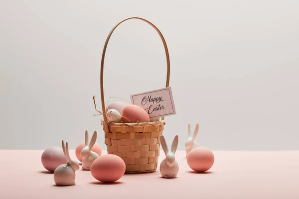 Easter chicken and quail egg in straw basket, toy rabbits and card with happy easter lettering — Stock Photo