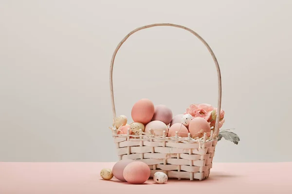 Eater chicken and quail eggs in straw basket with flower on grey background — Stock Photo