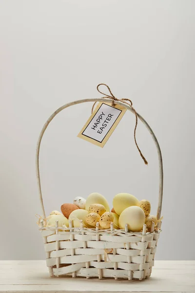 Easter chicken and quail eggs in straw basket with flower and card with happy easter lettering — Stock Photo