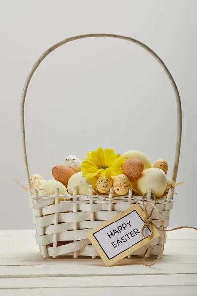 Poulet de Pâques et oeufs de caille dans le panier de paille avec fleur et carte avec joyeuse lettre de Pâques sur la table — Photo de stock