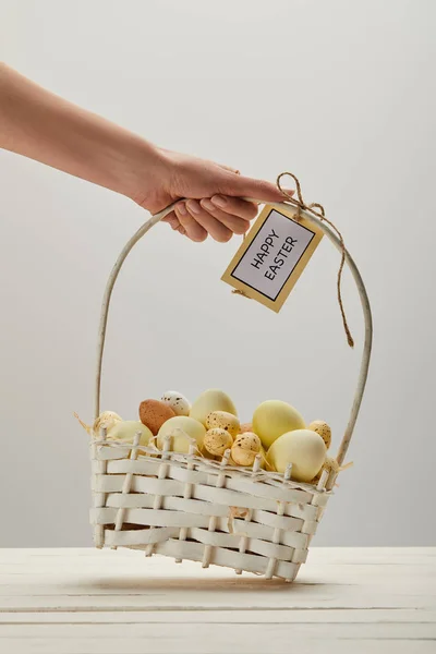 Vista cortada da mulher segurando cesta de palha com ovos de galinha e codorna de Páscoa, cartão com letras felizes de Páscoa — Fotografia de Stock