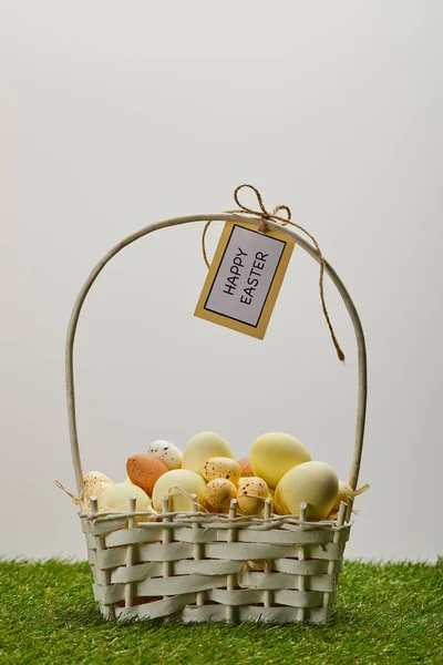 Easter chicken and quail eggs in straw basket with flower and card with happy easter lettering on grass — Stock Photo