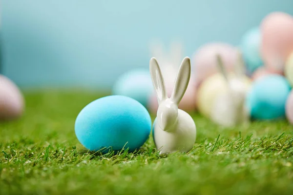 Foco seletivo de ovos de páscoa pintados e coelhos de brinquedo na grama com espaço de cópia — Fotografia de Stock
