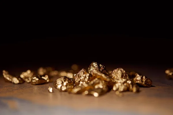 Selective focus of golden stones on grey and brown marble surface with blurred black background — Stock Photo