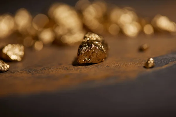 Селективный фокус золотых камней на серой и коричневой мраморной поверхности с размытым фоном — стоковое фото