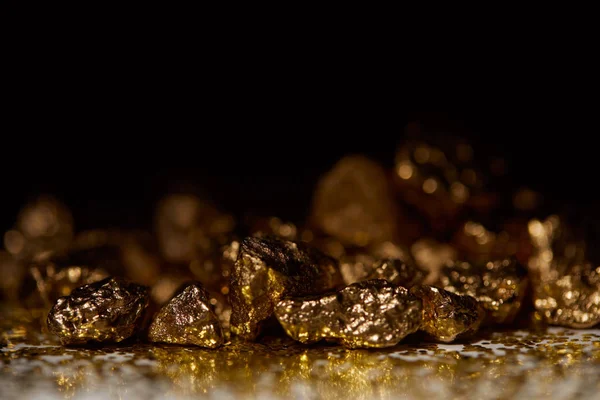 Enfoque selectivo de piedras doradas en la oscuridad sobre la superficie brillante y el fondo negro - foto de stock