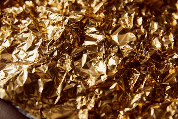 Geknitterte Goldfolie mit Funkeln auf brauner Oberfläche — Stockfoto