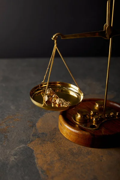 Golden stones on scales on marble table and black background — Stock Photo