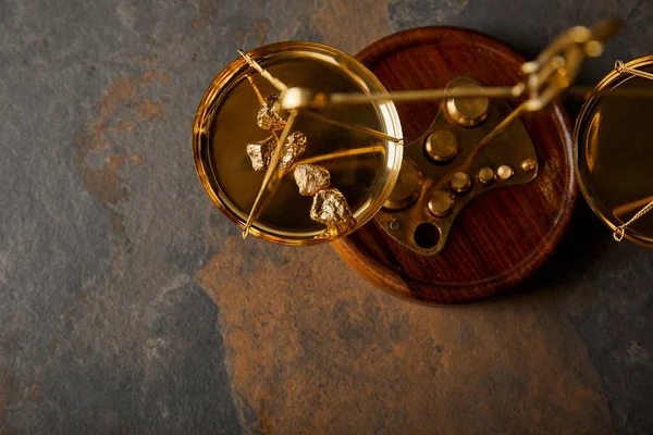 Top view of golden stones on scales on grey and brown marble table — Stock Photo