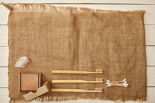 Top view of different hygiene and care items arranged on sackcloth on white wooden surface, zero waste concept — Stock Photo