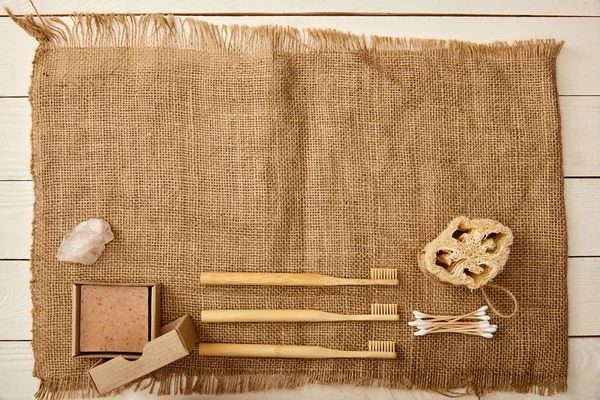 Top view of various hygiene and care items arranged on canvas on white wooden surface, zero waste concept — Stock Photo