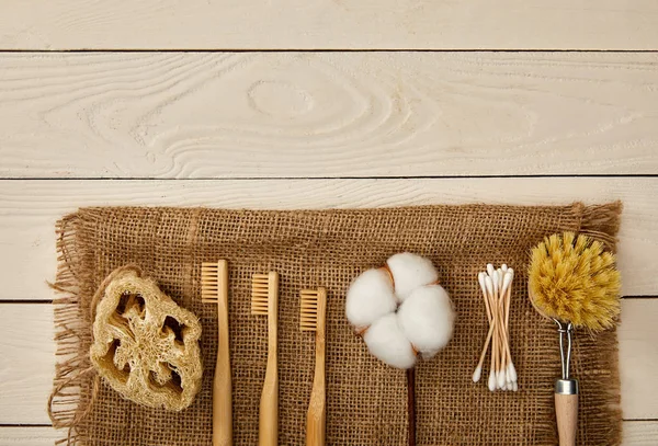 Flat lay of  hygiene and care items arranged on sackcloth on white wooden surface, zero waste concept — Stock Photo