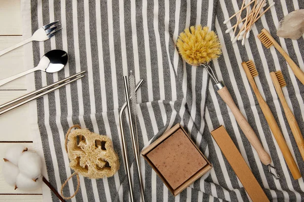 Top view of cutlery, hygiene and care items on striped towel on white wooden surface, zero waste concept — Stock Photo