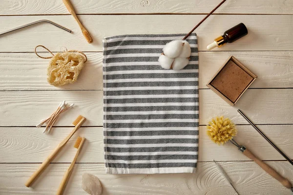 Top view of various hygiene and care items, and striped towel on white wooden surface, zero waste concept — Stock Photo