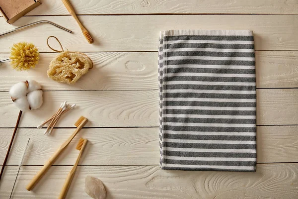 Top view of different hygiene and care items and striped towel on white wooden surface, zero waste concept — Stock Photo