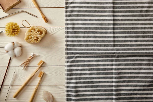 Draufsicht auf verschiedene Hygiene- und Pflegeartikel und gestreiftes Handtuch auf weißer Holzoberfläche, Zero-Waste-Konzept — Stockfoto