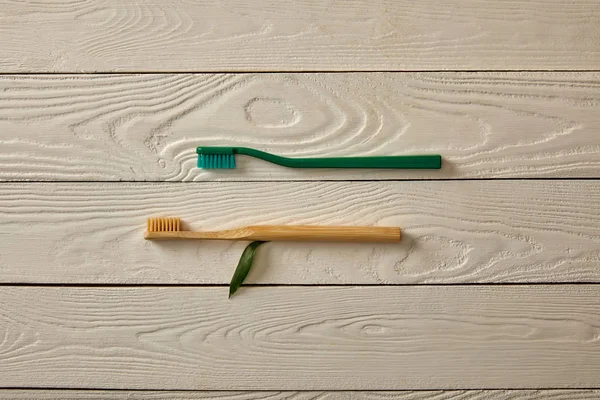 Top view of toothbrushes and green leaf on white wooden surface, zero waste concept — Stock Photo