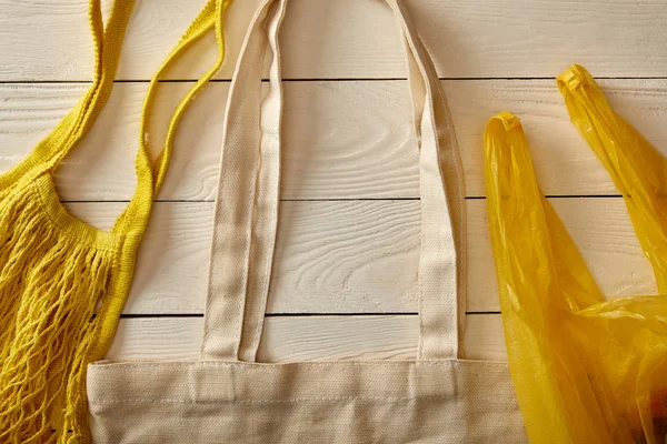 Vista superior do saco de algodão têxtil, saco de cordas e saco de plástico na superfície de madeira branca, conceito de desperdício zero — Fotografia de Stock
