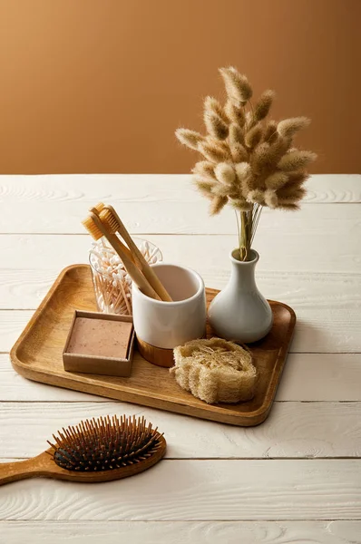 Haarbürste, Holztablett mit Vase aus Stacheln und verschiedenen Hygiene- und Pflegeartikeln auf weißer Holzoberfläche, Zero-Waste-Konzept — Stockfoto