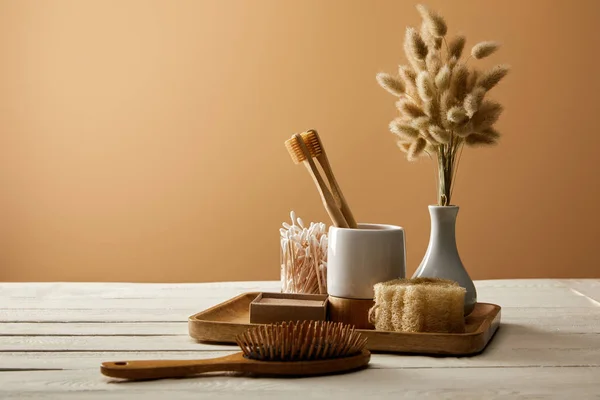 Bandeja de madera con diferentes artículos de higiene y cuidado, jarrón de espiguillas y cepillo para el cabello en la superficie de madera blanca, concepto de cero residuos - foto de stock