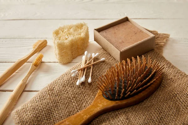 Diferentes artículos de higiene y cuidado sobre tela de saco en la superficie de madera blanca, concepto de cero residuos - foto de stock