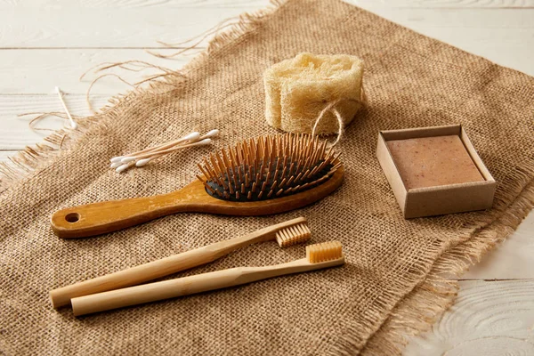 Diferentes artículos de higiene y cuidado sobre tela de saco en la superficie de madera blanca, concepto de cero residuos — Stock Photo