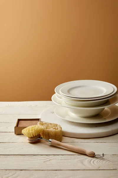 Stack of plates and various cleaning items on white wooden surface, zero waste concept — Stock Photo