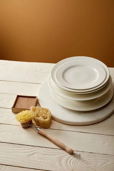 Stacked plates and various cleaning items on white wooden surface, zero waste concept — Stock Photo