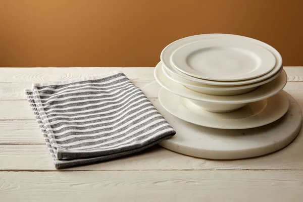 Stack of white plates and striped cotton towel on white wooden surface — Stock Photo